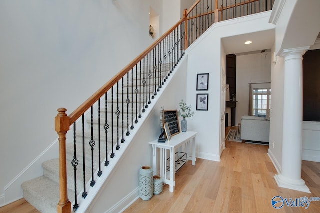 staircase featuring a towering ceiling, wood-type flooring, and ornate columns