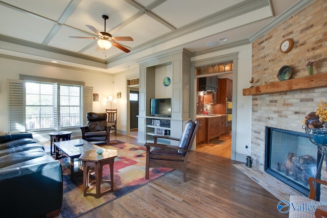 living room featuring ceiling fan, wood-type flooring, a fireplace, and ornamental molding