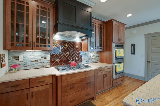 kitchen with light stone counters, decorative backsplash, light hardwood / wood-style flooring, and appliances with stainless steel finishes