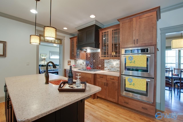 kitchen featuring stainless steel appliances, ornamental molding, hanging light fixtures, and a center island with sink