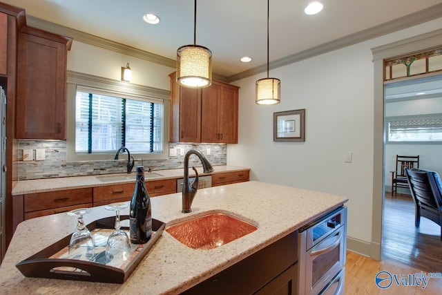 kitchen featuring pendant lighting, crown molding, light stone countertops, and sink