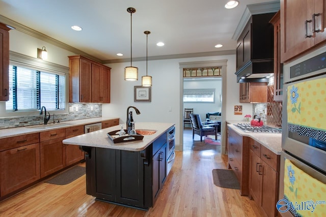 kitchen with sink, crown molding, decorative light fixtures, an island with sink, and light hardwood / wood-style floors