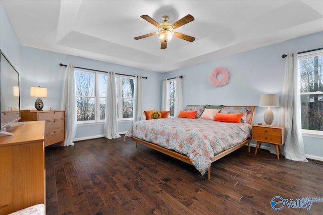 bedroom with ceiling fan, a tray ceiling, and dark hardwood / wood-style floors