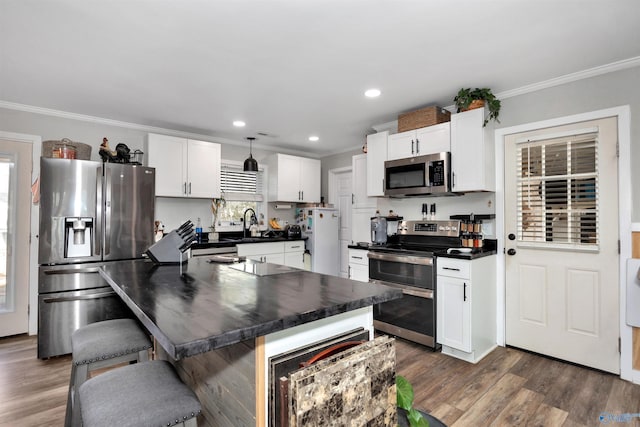 kitchen with dark wood-type flooring, appliances with stainless steel finishes, a kitchen breakfast bar, ornamental molding, and white cabinets