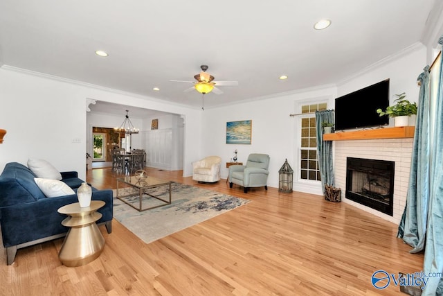 living room with crown molding, hardwood / wood-style floors, ceiling fan with notable chandelier, and a brick fireplace