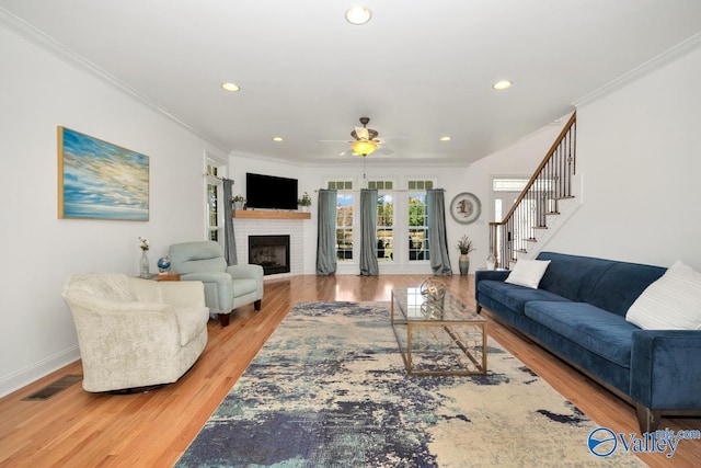 living room with crown molding, hardwood / wood-style floors, a brick fireplace, and ceiling fan