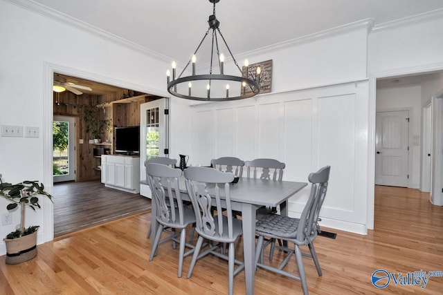 dining room with crown molding, wood walls, light wood-type flooring, and ceiling fan with notable chandelier