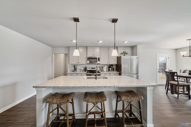 kitchen with a kitchen bar, appliances with stainless steel finishes, pendant lighting, and an island with sink