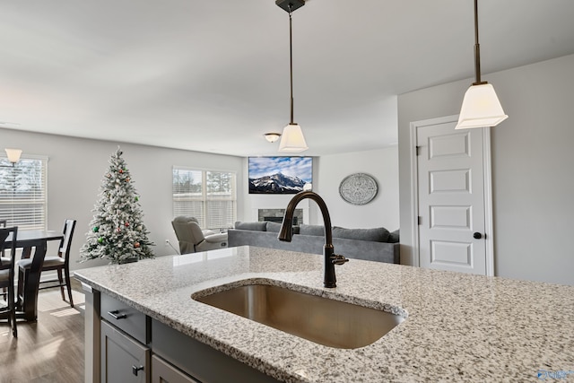 kitchen with light stone countertops, sink, decorative light fixtures, and light wood-type flooring