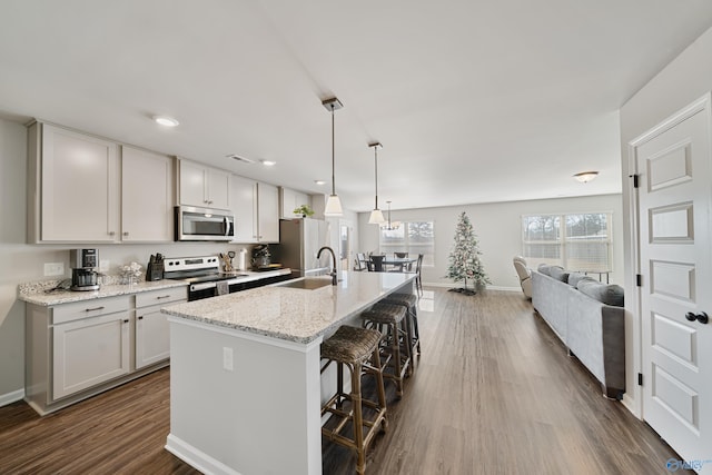 kitchen with a center island with sink, a kitchen breakfast bar, sink, appliances with stainless steel finishes, and light stone counters