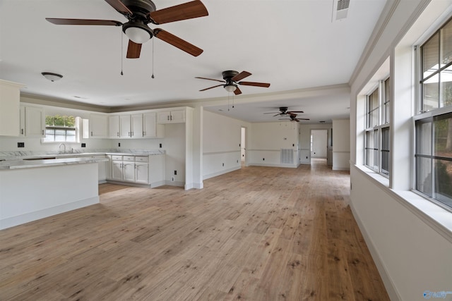 unfurnished living room featuring light wood-type flooring, sink, ceiling fan, and ornamental molding