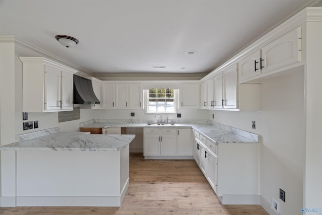 kitchen featuring white cabinetry, light wood-type flooring, sink, and wall chimney range hood