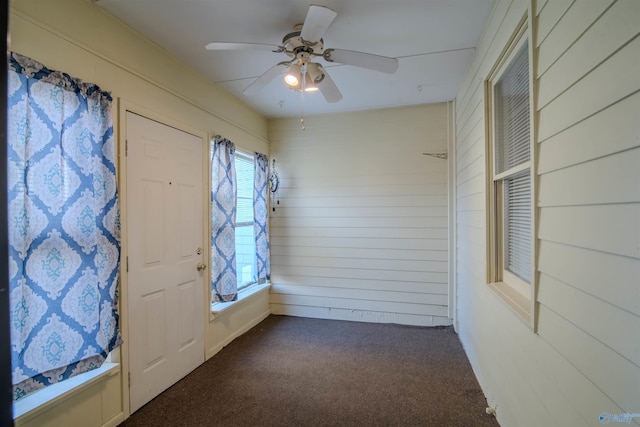 empty room with wood walls, ceiling fan, and dark colored carpet