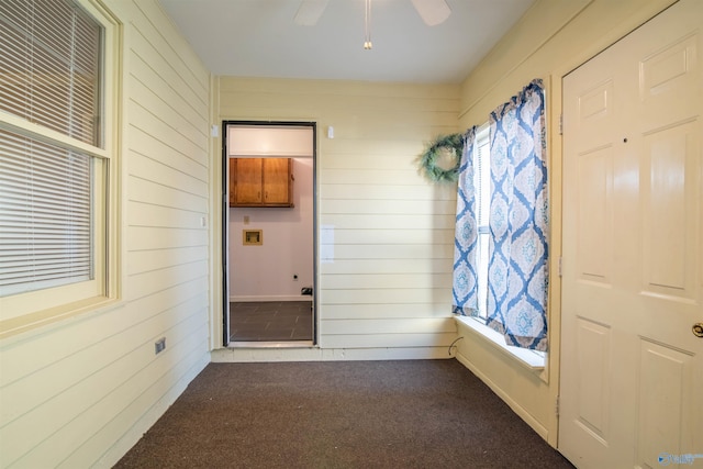 spare room with wooden walls, dark colored carpet, and ceiling fan