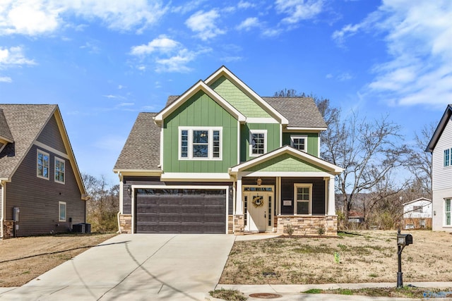 craftsman-style house featuring a shingled roof, concrete driveway, stone siding, a porch, and board and batten siding