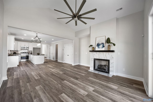 unfurnished living room featuring dark wood finished floors, visible vents, a high end fireplace, baseboards, and ceiling fan with notable chandelier