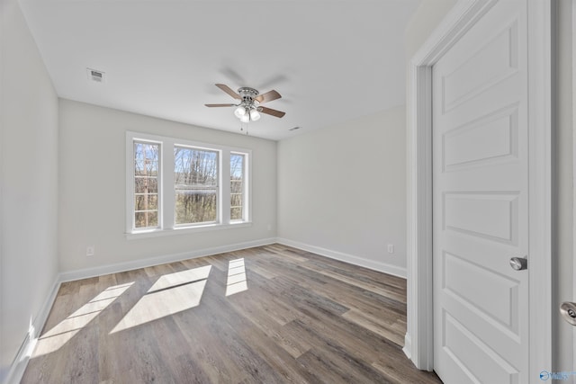 spare room featuring a ceiling fan, visible vents, baseboards, and wood finished floors