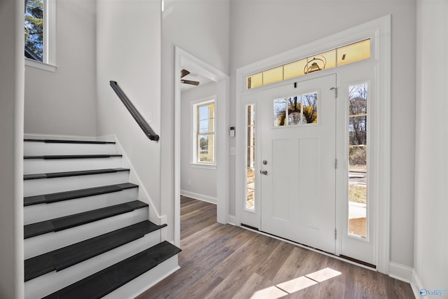 foyer with a healthy amount of sunlight, stairway, baseboards, and wood finished floors