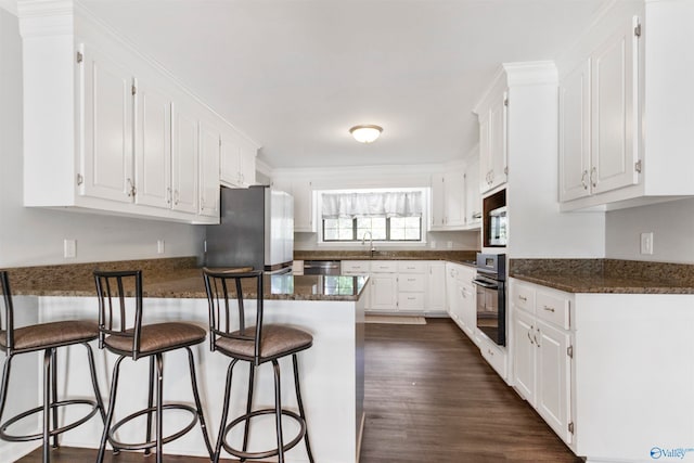 kitchen with dark hardwood / wood-style floors, dark stone counters, a breakfast bar area, white cabinets, and appliances with stainless steel finishes