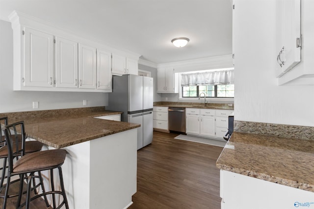 kitchen featuring white cabinets, a breakfast bar area, appliances with stainless steel finishes, and dark wood-type flooring