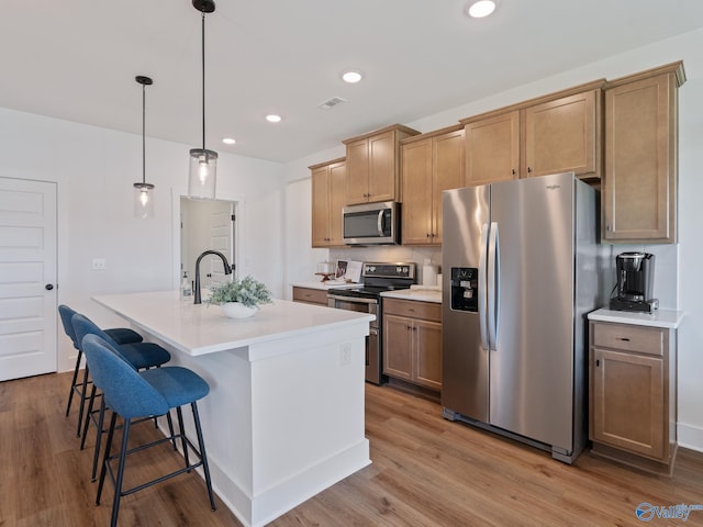 kitchen featuring appliances with stainless steel finishes, a breakfast bar, a kitchen island with sink, light wood-type flooring, and decorative light fixtures