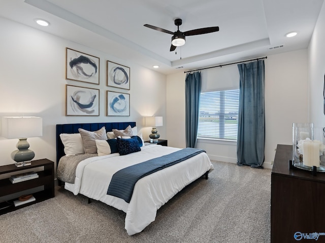 carpeted bedroom with a raised ceiling and ceiling fan