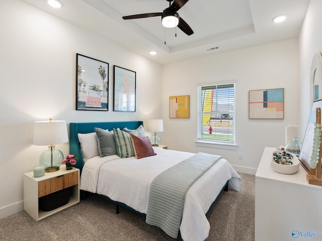 carpeted bedroom featuring a tray ceiling and ceiling fan