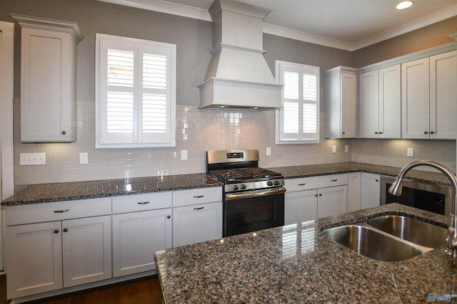 kitchen featuring dark stone countertops, stainless steel range with gas cooktop, backsplash, and custom range hood