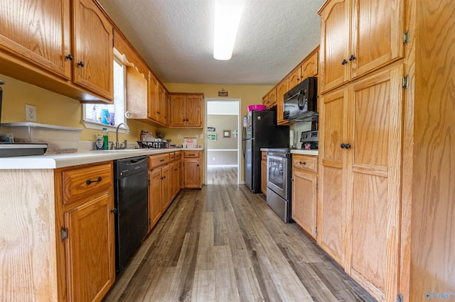 207 Sharp Dr, Gadsden, AL 35903 - kitchen featuring black appliances, light wood-style flooring, light countertops, a sink, and a textured ceiling