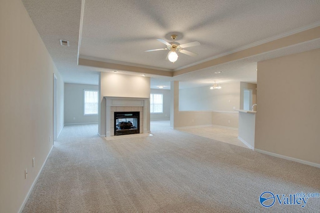 unfurnished living room featuring a textured ceiling, ceiling fan, light colored carpet, crown molding, and a tiled fireplace