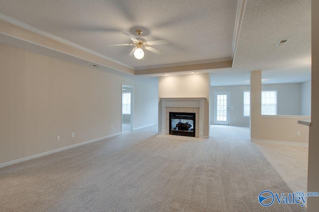 unfurnished living room featuring ceiling fan, a tile fireplace, a tray ceiling, crown molding, and light carpet