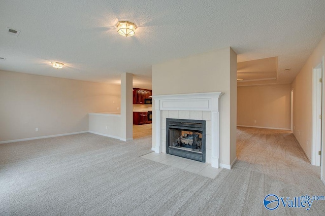 unfurnished living room with a textured ceiling, light colored carpet, and a tiled fireplace