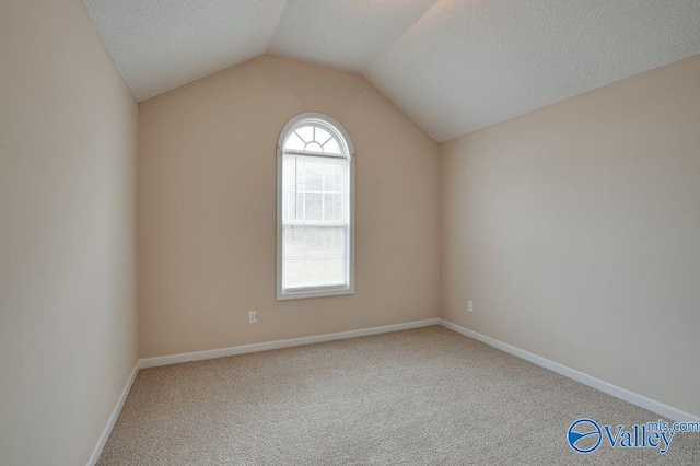 empty room with carpet, vaulted ceiling, and a textured ceiling