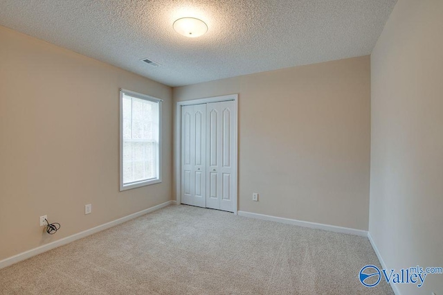 unfurnished bedroom featuring light colored carpet, a textured ceiling, and a closet