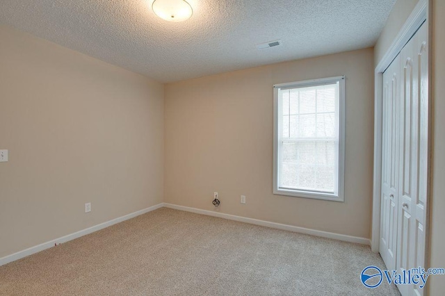 unfurnished bedroom with light carpet, a closet, and a textured ceiling