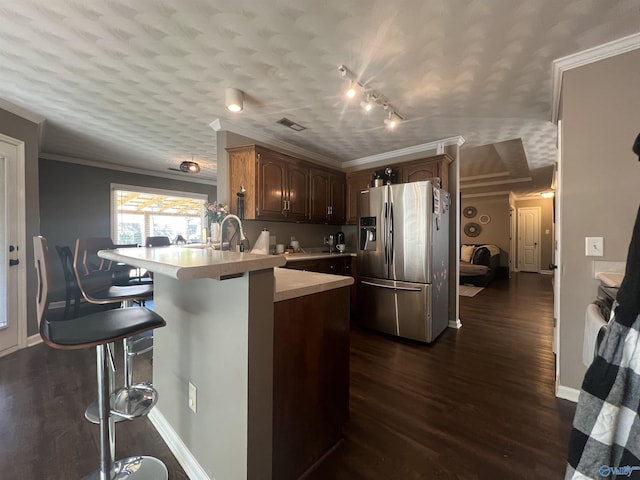 kitchen with dark wood-style floors, a peninsula, stainless steel fridge with ice dispenser, light countertops, and a kitchen breakfast bar