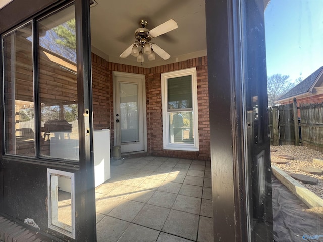 view of exterior entry with a patio area, fence, a ceiling fan, and brick siding