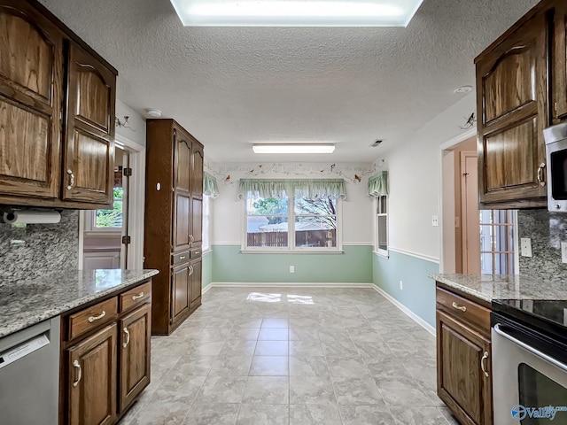 kitchen featuring a healthy amount of sunlight, decorative backsplash, stainless steel appliances, and light stone countertops