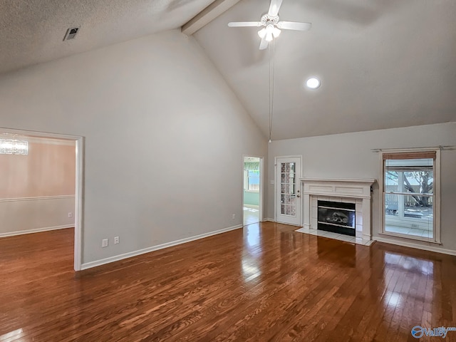 unfurnished living room with a tiled fireplace, beamed ceiling, a textured ceiling, ceiling fan, and hardwood / wood-style floors