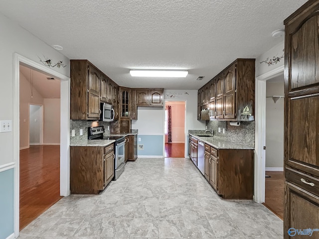 kitchen featuring a textured ceiling, dark brown cabinets, stainless steel appliances, and tasteful backsplash