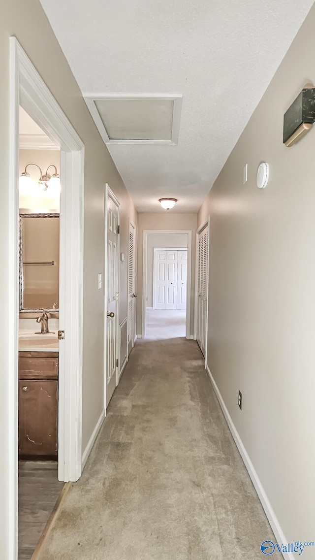 hall with light carpet, attic access, and baseboards