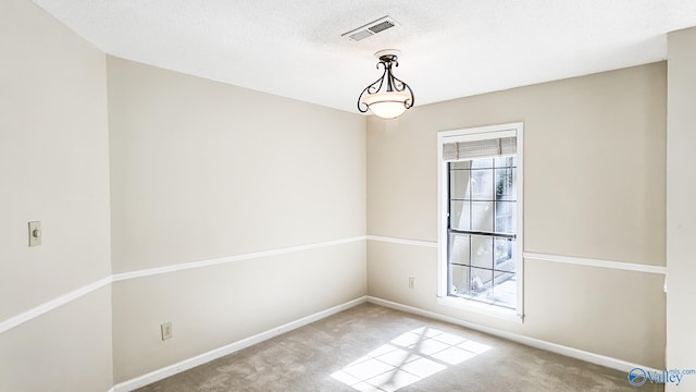 empty room featuring a textured ceiling, carpet floors, visible vents, and baseboards