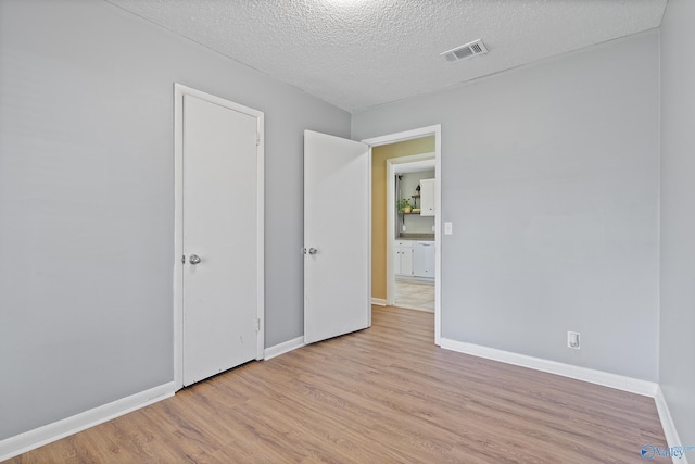 unfurnished bedroom with baseboards, wood finished floors, visible vents, and a textured ceiling