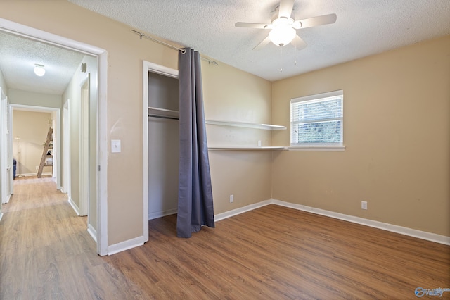 unfurnished bedroom featuring baseboards, wood finished floors, a textured ceiling, and a closet