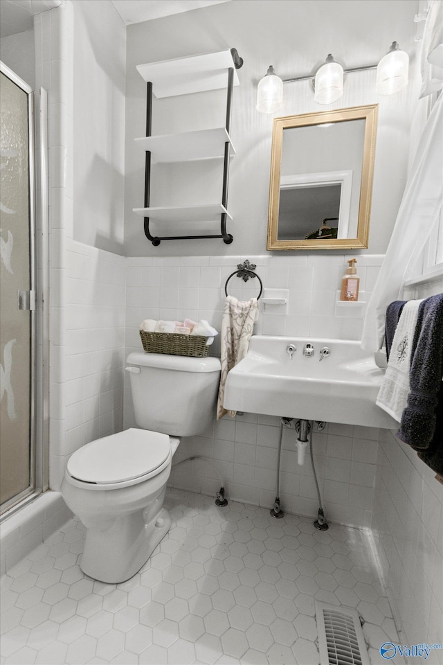 bathroom featuring tile walls, a shower with door, toilet, and tile patterned floors