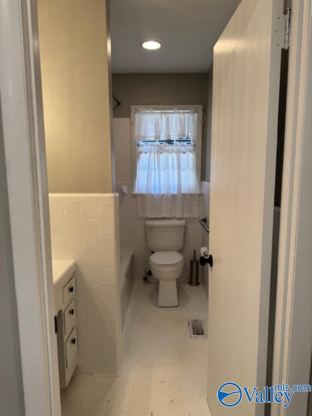 bathroom with toilet, tile walls, and vanity