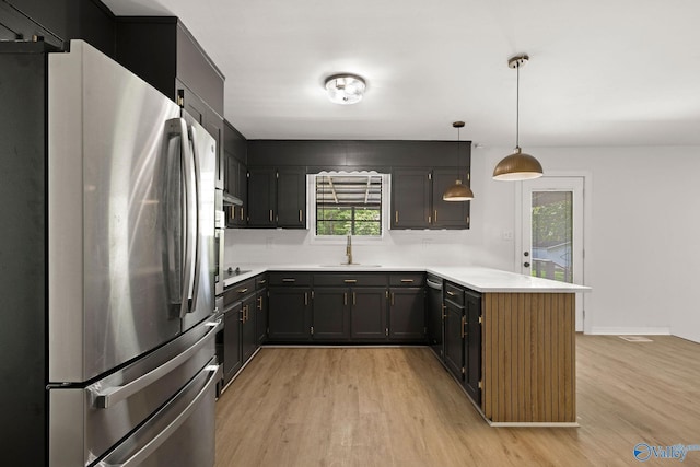 kitchen featuring freestanding refrigerator, a peninsula, light countertops, a sink, and light wood finished floors