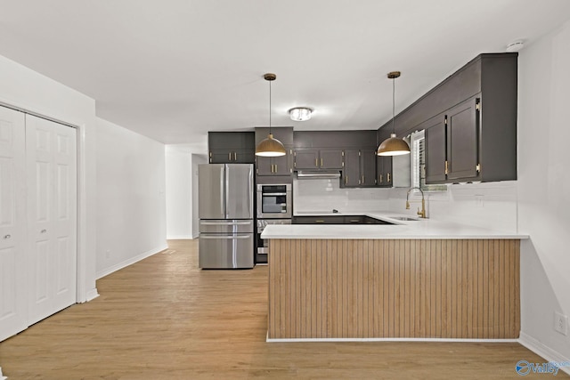 kitchen with appliances with stainless steel finishes, light wood-type flooring, a sink, a peninsula, and under cabinet range hood