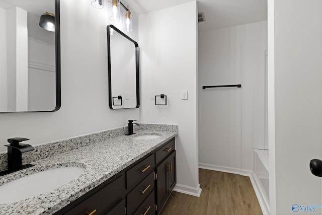 full bath featuring double vanity, a sink, baseboards, and wood finished floors