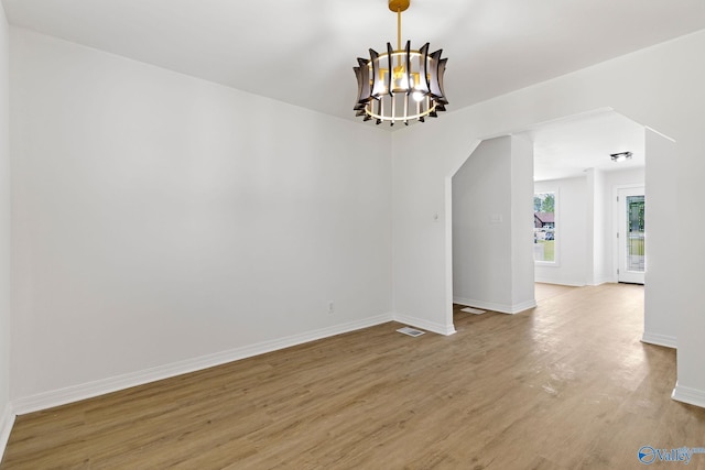 spare room with baseboards, a chandelier, visible vents, and light wood-type flooring